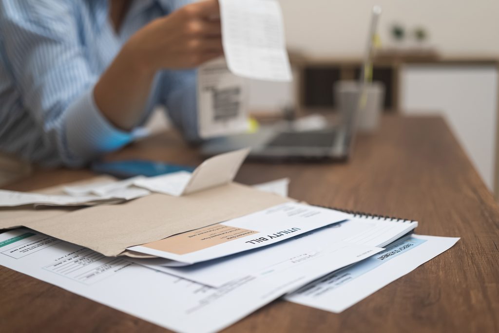 Utility bills with total amount for payment on wooden surface against woman examining bank documents - Kings Plumbing water leak and water bill showing money being drained